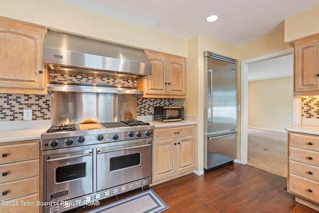 kitchen with high quality appliances, light brown cabinetry, dark wood-style floors, wall chimney exhaust hood, and light countertops