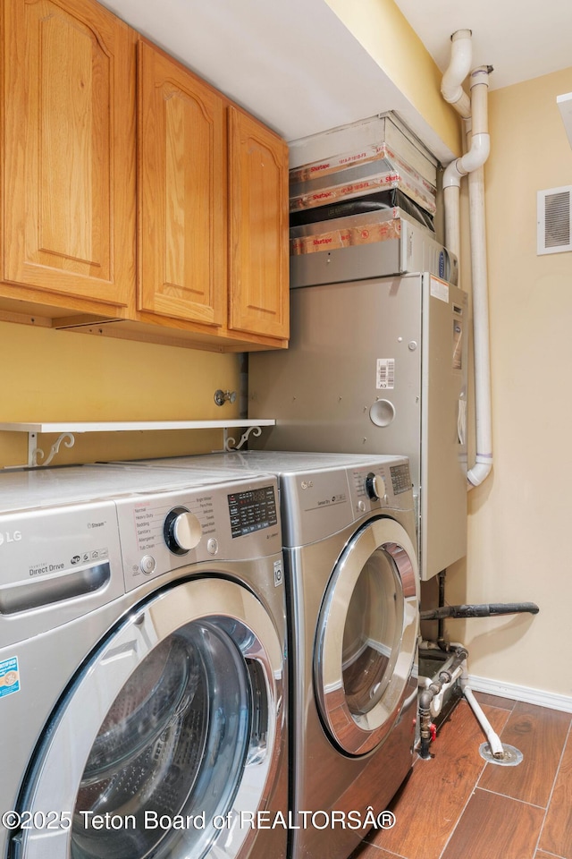 clothes washing area featuring visible vents, washer and clothes dryer, wood finished floors, cabinet space, and baseboards