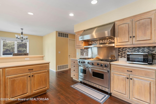 kitchen featuring visible vents, light countertops, wall chimney exhaust hood, and range with two ovens