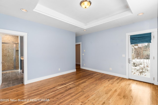 empty room featuring a raised ceiling, wood finished floors, and baseboards
