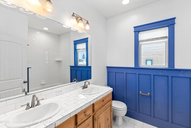 full bath with plenty of natural light, wainscoting, toilet, and a sink