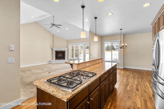 kitchen featuring light stone counters, open floor plan, a center island, stainless steel appliances, and lofted ceiling