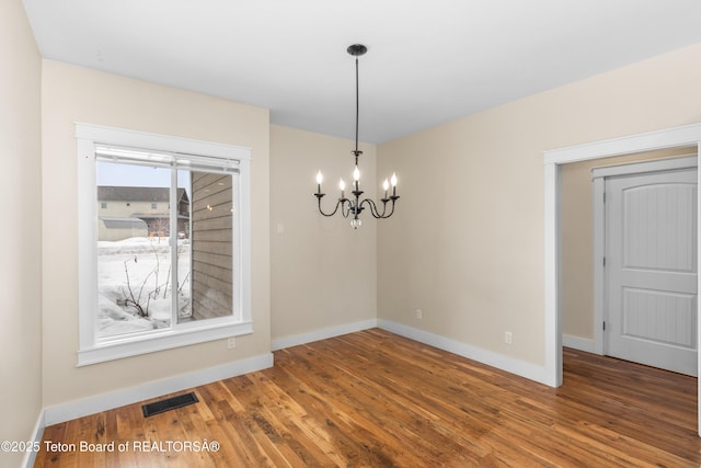 empty room with a notable chandelier, visible vents, baseboards, and wood finished floors