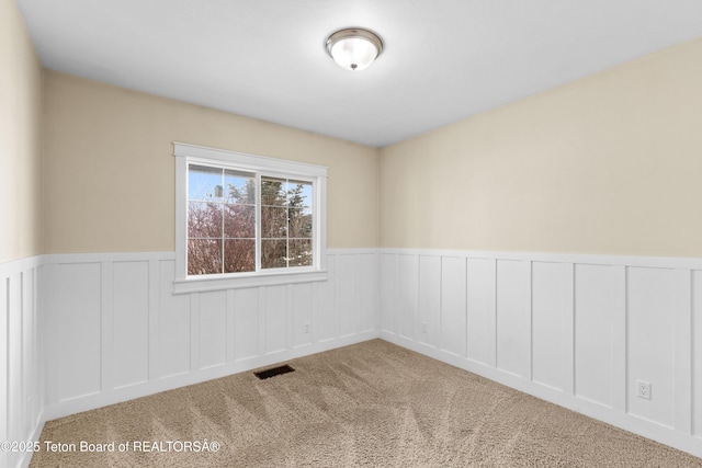 empty room featuring visible vents, wainscoting, and carpet flooring