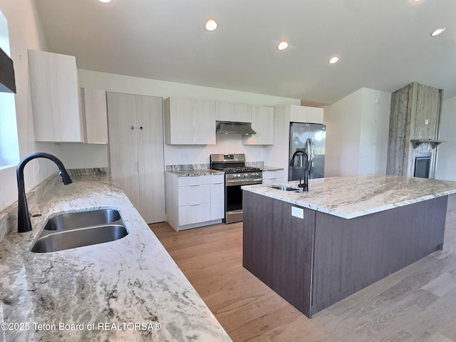 1714 River Meadows Dr, Victor, ID 83455 - kitchen featuring stainless steel appliances, under cabinet range hood, a center island with sink, light wood finished floors, and light stone countertops