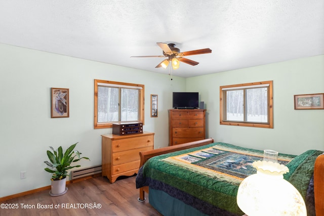 bedroom with baseboards, wood finished floors, a textured ceiling, a ceiling fan, and a baseboard radiator