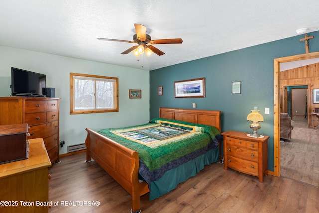 bedroom featuring baseboard heating, wood finished floors, and a ceiling fan
