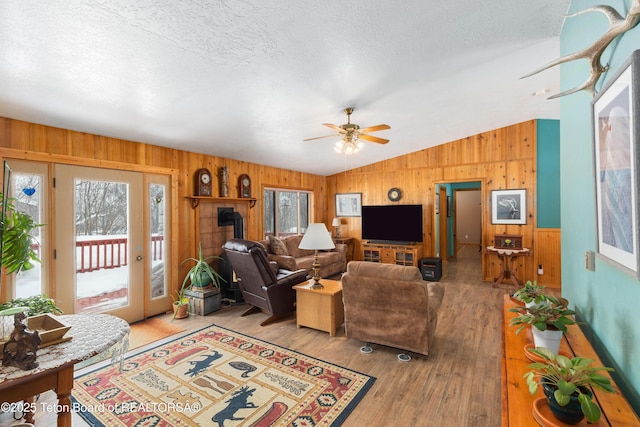 living area with wooden walls, a ceiling fan, lofted ceiling, a textured ceiling, and light wood-type flooring