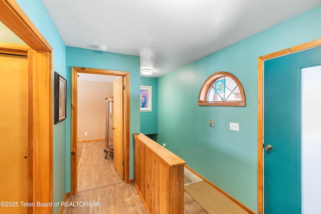 corridor with light wood-type flooring, baseboards, a textured ceiling, and an upstairs landing