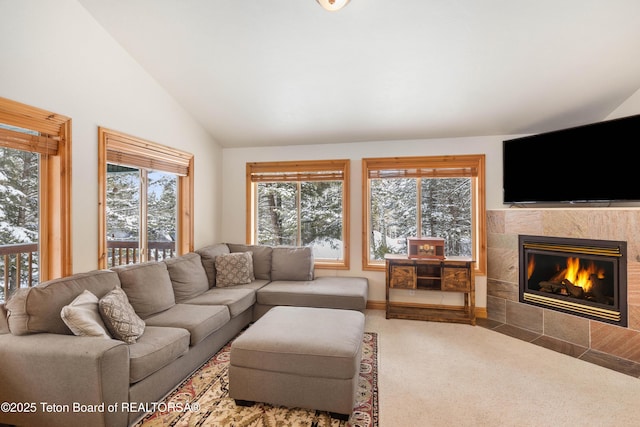 carpeted living area featuring a tiled fireplace, vaulted ceiling, and a wealth of natural light