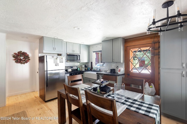 kitchen featuring light wood finished floors, dark countertops, appliances with stainless steel finishes, gray cabinetry, and backsplash