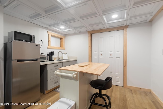 kitchen featuring wooden counters, a sink, black microwave, coffered ceiling, and freestanding refrigerator