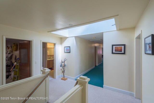 hallway featuring baseboards, an upstairs landing, and carpet