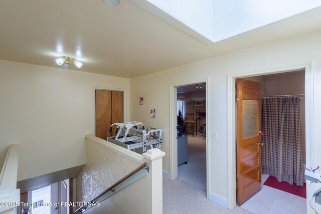 hallway with an upstairs landing, a skylight, and baseboards