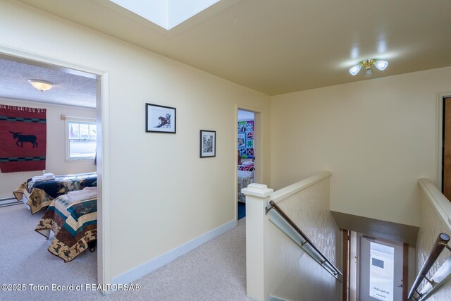 hall with baseboards, an upstairs landing, carpet floors, and a textured ceiling