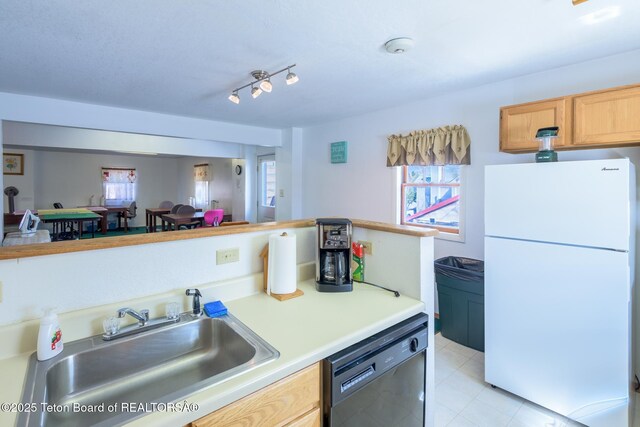 kitchen with light tile patterned flooring, light countertops, a sink, freestanding refrigerator, and black dishwasher