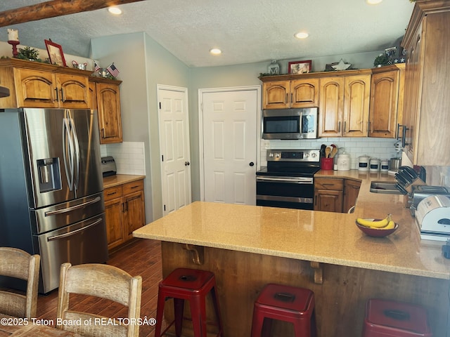 kitchen with brown cabinetry, a peninsula, appliances with stainless steel finishes, and a breakfast bar area