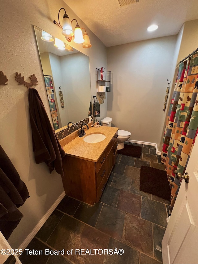 bathroom with vanity, baseboards, toilet, visible vents, and stone finish flooring