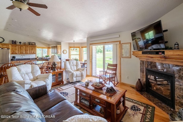 living room with ceiling fan, a high end fireplace, a textured ceiling, vaulted ceiling, and light wood-style flooring