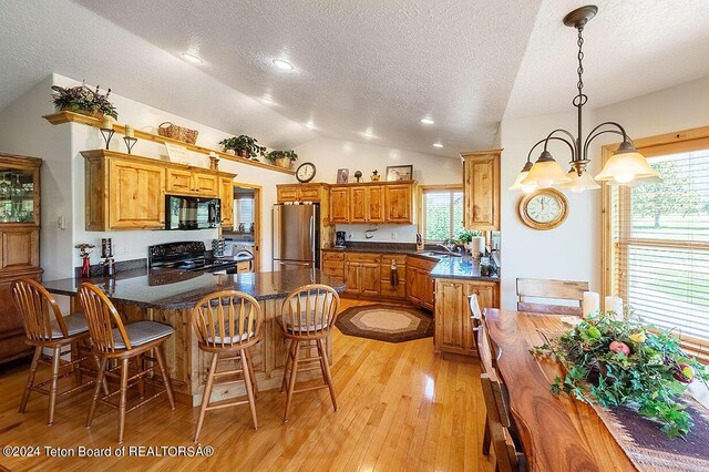 kitchen with a sink, a peninsula, light wood finished floors, black appliances, and lofted ceiling