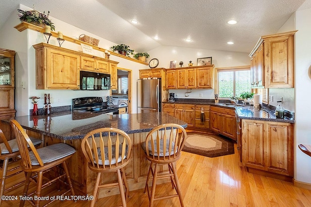 kitchen with a sink, light wood-type flooring, a peninsula, black appliances, and vaulted ceiling