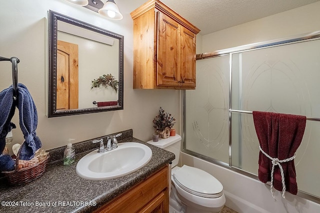 bathroom featuring toilet, a textured ceiling, vanity, and bath / shower combo with glass door