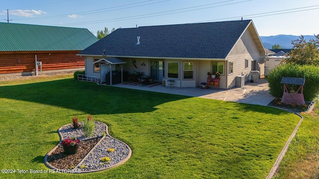 rear view of house with a patio area, a mountain view, a yard, and roof with shingles