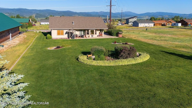 rear view of house with a patio area, a mountain view, and a lawn
