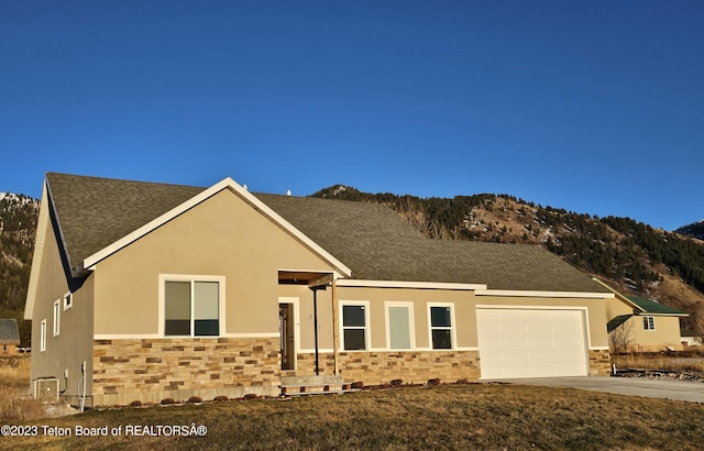 view of front of property with concrete driveway, stucco siding, a mountain view, stone siding, and an attached garage