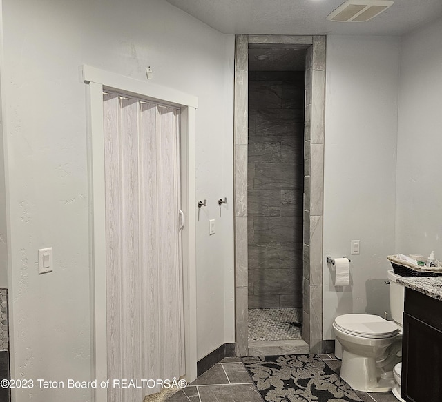 bathroom with toilet, tiled shower, vanity, and visible vents