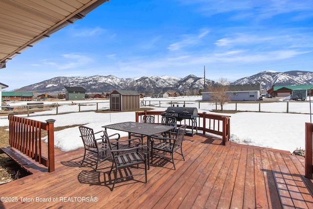 snow covered deck with an outdoor structure, outdoor dining area, a mountain view, and a shed