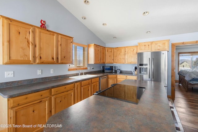 kitchen with dark countertops, a sink, a kitchen breakfast bar, stainless steel appliances, and vaulted ceiling