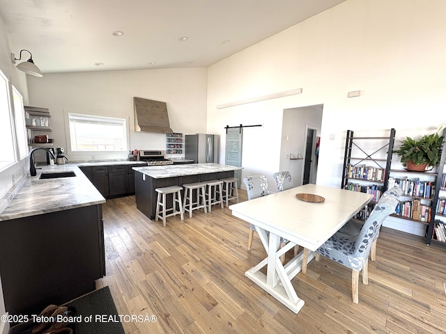 dining area featuring light wood-style flooring, high vaulted ceiling, a barn door, and recessed lighting