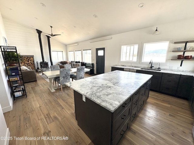 kitchen featuring a sink, open floor plan, a wood stove, dark cabinets, and lofted ceiling