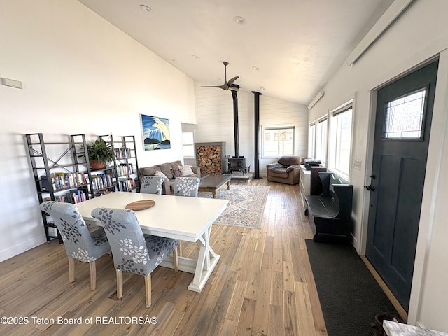 dining room with high vaulted ceiling, a wood stove, light wood finished floors, and baseboards