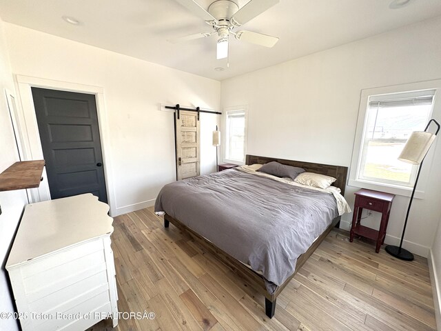 bedroom featuring light wood-style floors, ceiling fan, baseboards, and a barn door