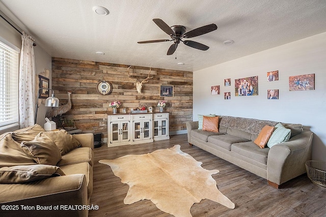 living area with plenty of natural light, wooden walls, wood finished floors, and a ceiling fan