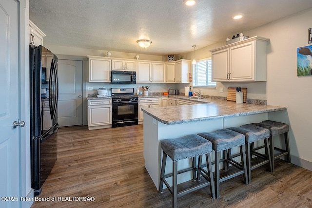 kitchen featuring a peninsula, a textured ceiling, dark wood finished floors, a breakfast bar, and black appliances