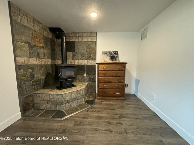 living area with dark wood-style flooring, a wood stove, visible vents, and baseboards