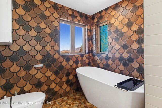 708 Palisades Ln, Alpine, WY 83128 - bathroom with a freestanding bath, stone finish floor, wallpapered walls, and toilet