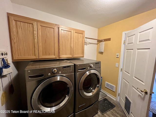 laundry area with separate washer and dryer, visible vents, wood finished floors, baseboards, and cabinet space