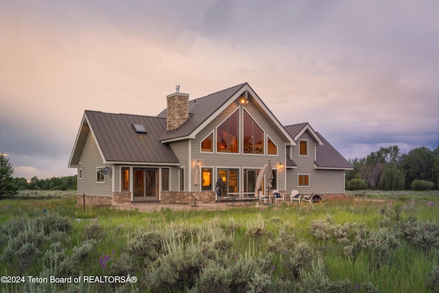 back of property at dusk featuring stone siding, a standing seam roof, a chimney, and metal roof
