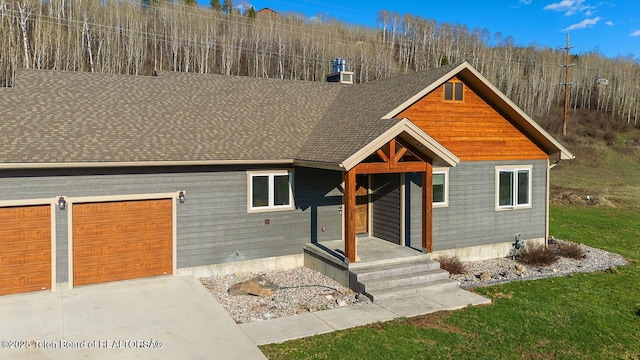 view of front of home with an attached garage, concrete driveway, a chimney, roof with shingles, and a front lawn