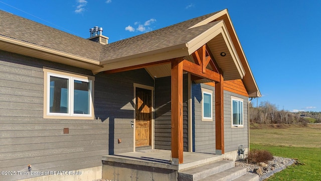 property entrance featuring roof with shingles and a lawn