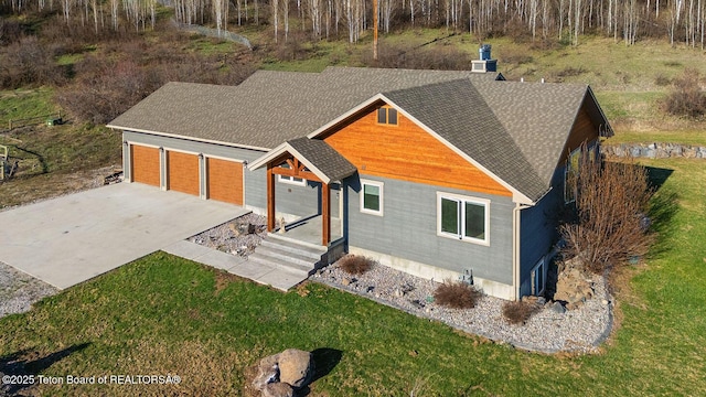 view of front of house with a front lawn, concrete driveway, roof with shingles, and a garage
