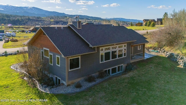 rear view of property with a mountain view, a chimney, a yard, and a shingled roof