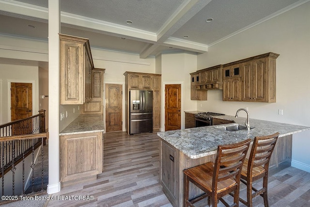 kitchen featuring stainless steel refrigerator with ice dispenser, gas range oven, a sink, a peninsula, and light wood-style flooring