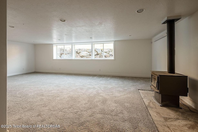 unfurnished living room featuring a wood stove, a textured ceiling, light carpet, and baseboards
