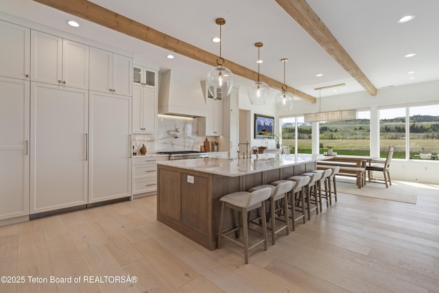 1070 Horseshoe Ln, Driggs, ID 83422 - kitchen featuring premium range hood, beam ceiling, light wood-style floors, white cabinetry, and a large island with sink