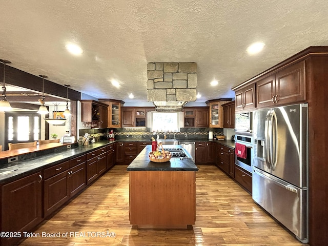 125 Wagon Rut Ln, Auburn, WY 83111 - kitchen with stainless steel appliances, dark countertops, a kitchen island, light wood finished floors, and a textured ceiling
